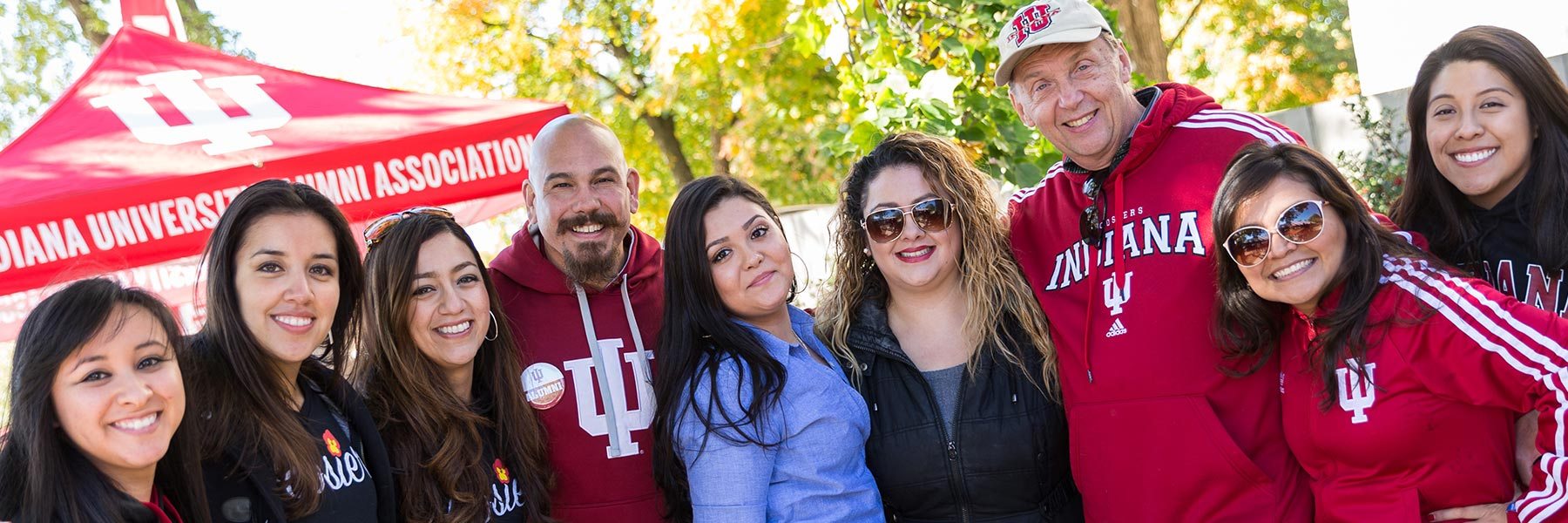 A group of people stand side by side smiling in front of an Indiana University tent