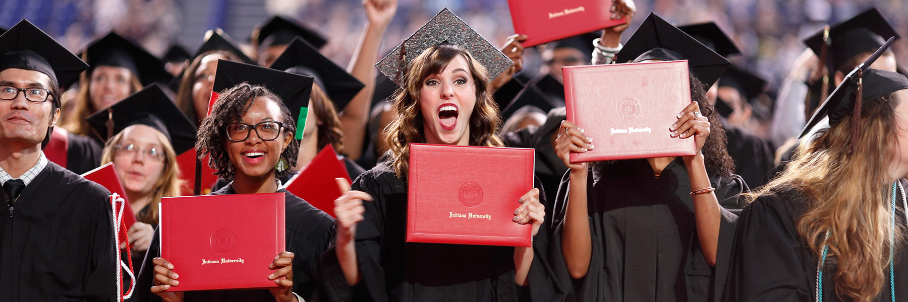 A group of people in graduation caps and gowns stand holding their IU diplomas